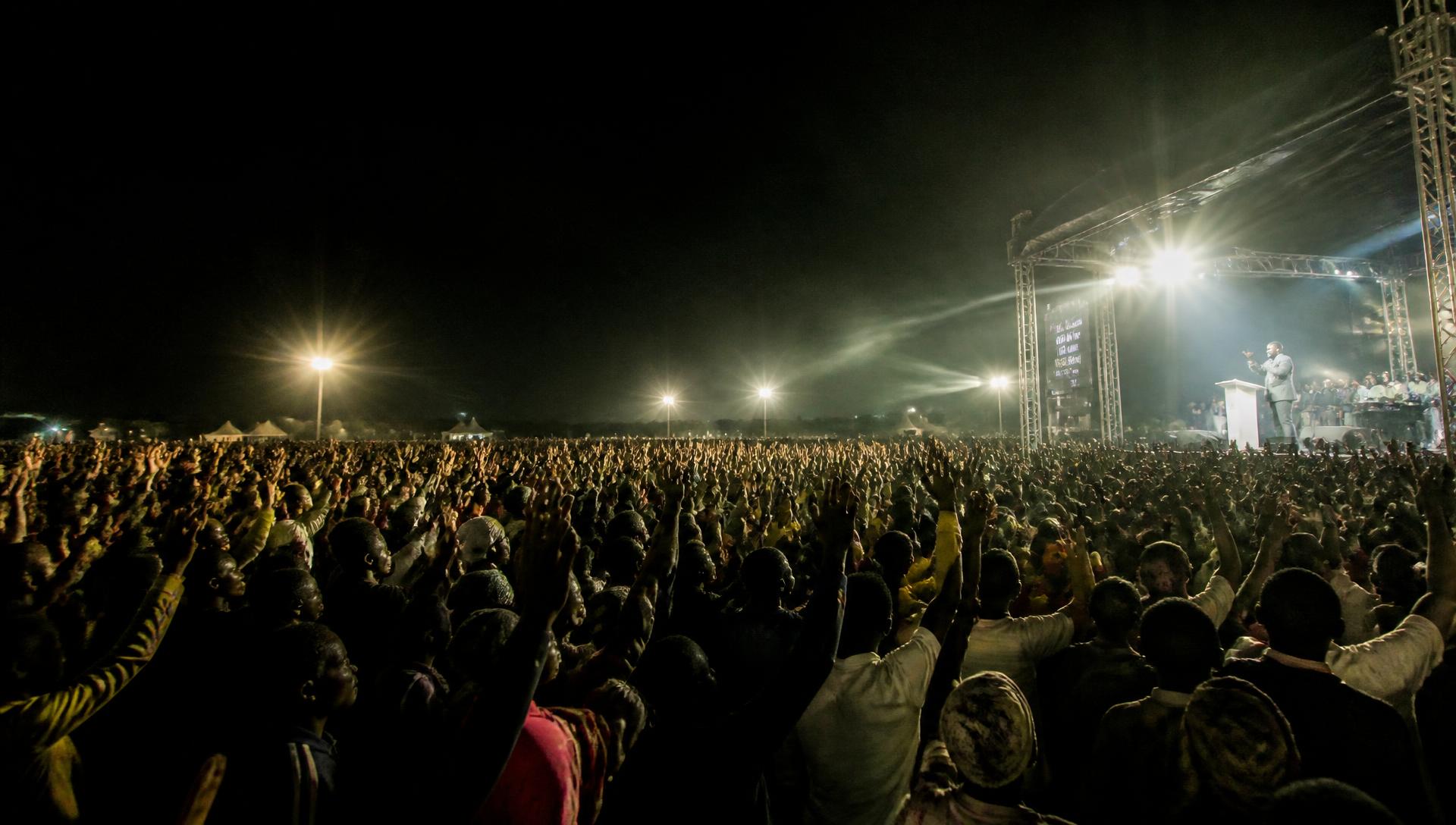 Crowds with raised hands at a floodlit open-air gospel crusade at night